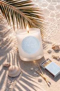 Candle with a label on sand and shells, palm leaf