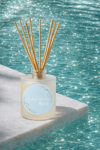 Reed diffuser with wooden sticks in a clear bottle against a sparkling water background