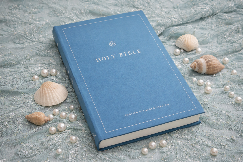 Blue Bible on a textured surface with pearls and shells