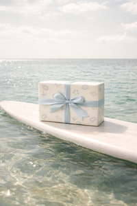 Gift box with a blue ribbon on a surfboard over water