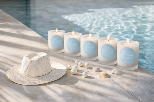 Set of candles with blue labels next to a hat and shells by a pool